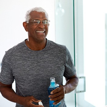 Senior man smiling in mirror while holding mouthwash