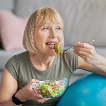 Senior woman smiling while eating salad at home