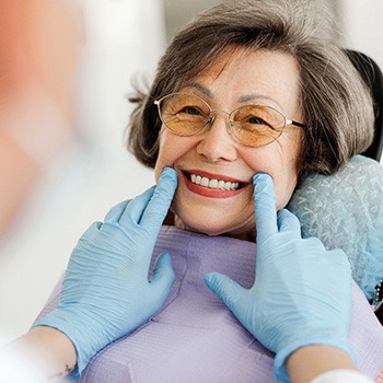 Dentist with blue gloves looking at senior woman's smile