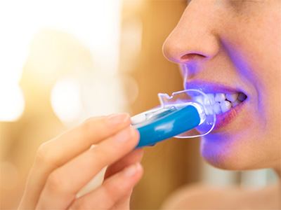 Nost-to-neck view of someone applying take-home whitening light to their teeth