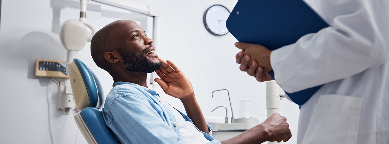Male dental patient touching jaw and looking up at dentist