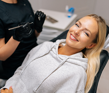 Woman in grey hoodie sitting back in dental chair and smiling