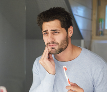 Man holding toothbrush and rubbing jaw in pain